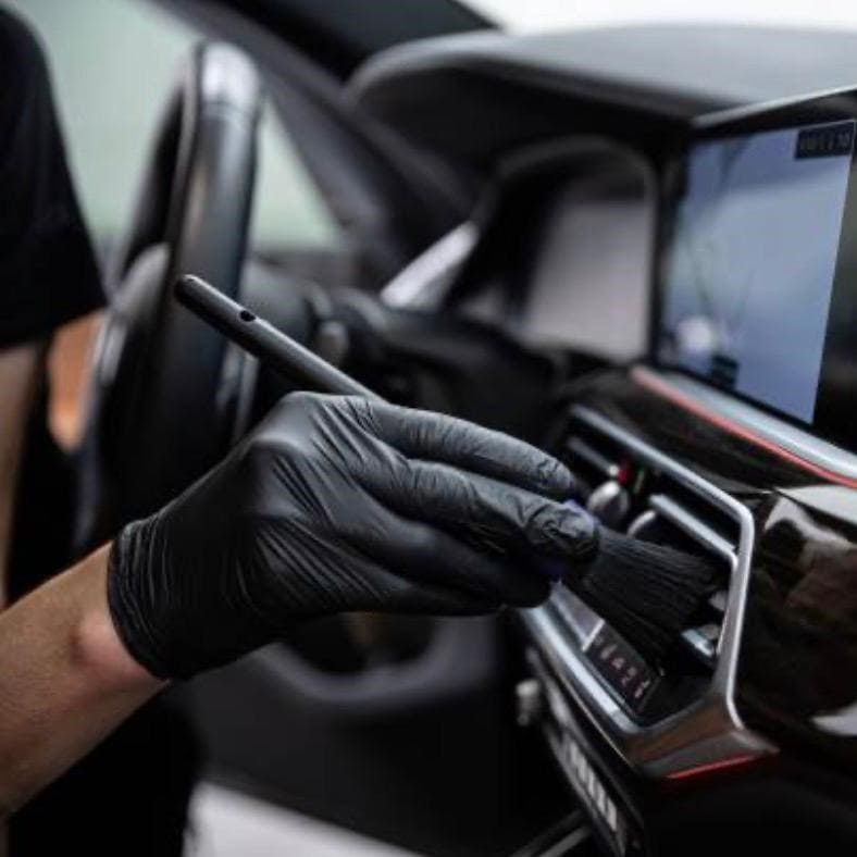 Ein Detailer säubert mit einem speziellen Reinigungspinsel vorsichtig die Lüftungsdüsen im modernen Fahrzeug-Interieur.