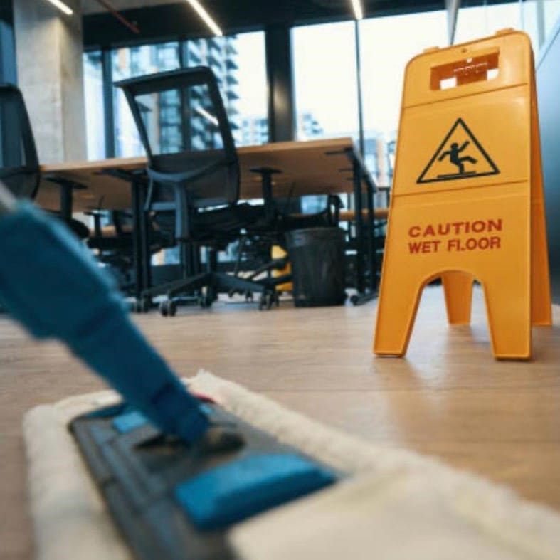 Professionelle Büroreinigung: Reinigungsservice wischt den Boden in einem modernen Großraumbüro, gesichert durch ein gelbes Warnschild für Rutschgefahr.